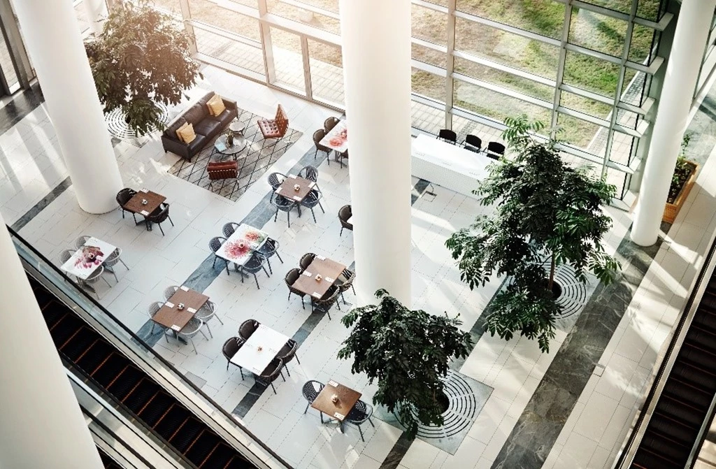 View from an internal balcony inside a high-rise, smart building using Azure IoT looking down on a light-filled lobby filled with tables, chairs, and plants.