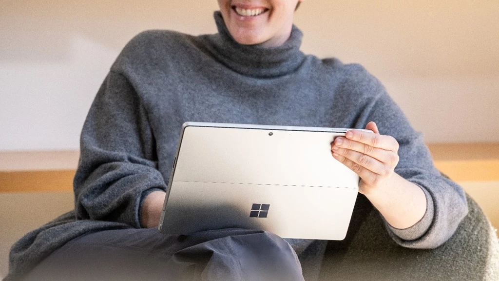 A woman is smiling while using a Microsoft surface to explore Microsoft skilling offerings to advance her learning.