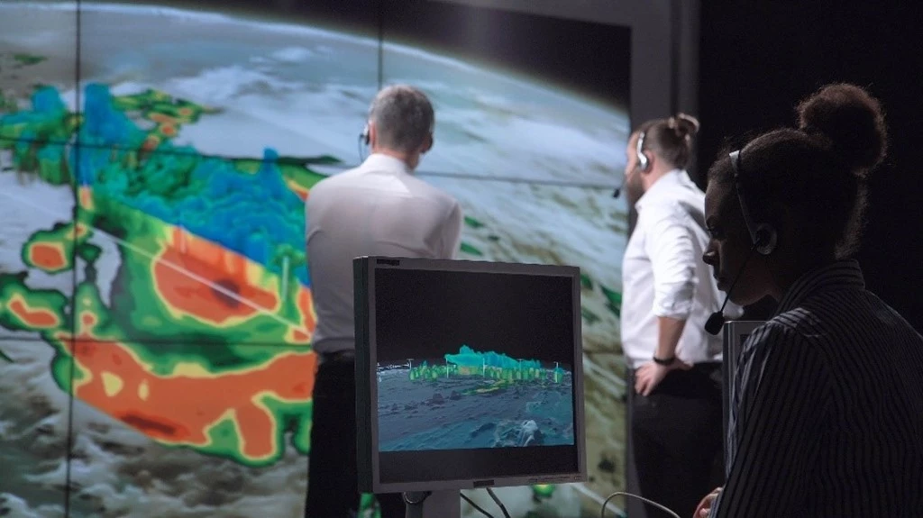 Image of 3 people analyzing weather on a large screen and smaller monitor