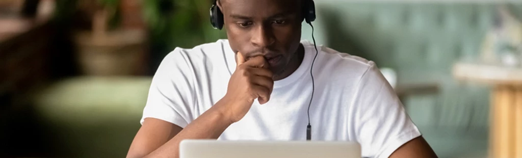 Photograph of man with headphones on in front of laptop with screen open. 