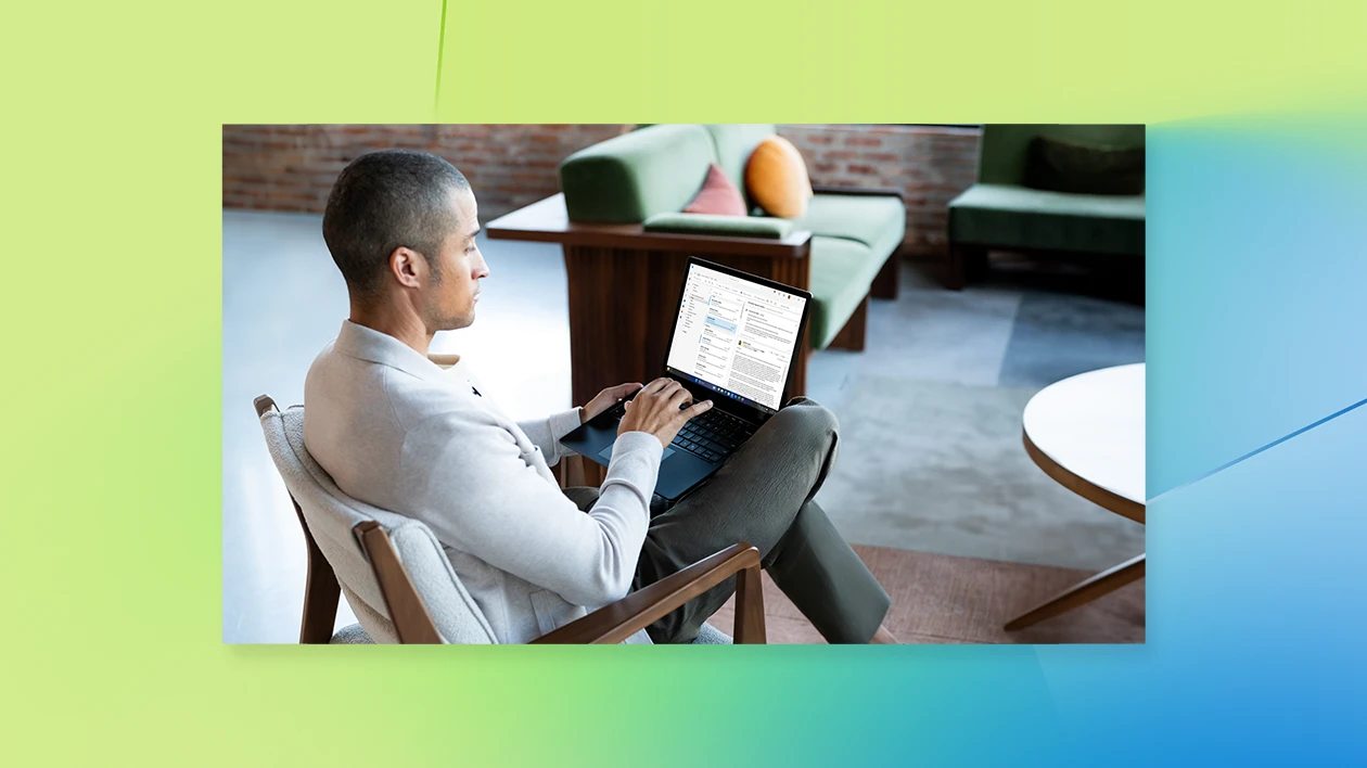 Photograph of male sitting on lobby chair collaborating on a Surface Laptop 6 in Black.