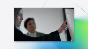 Engineer pointing at code displayed on a large monitor in an office environment.