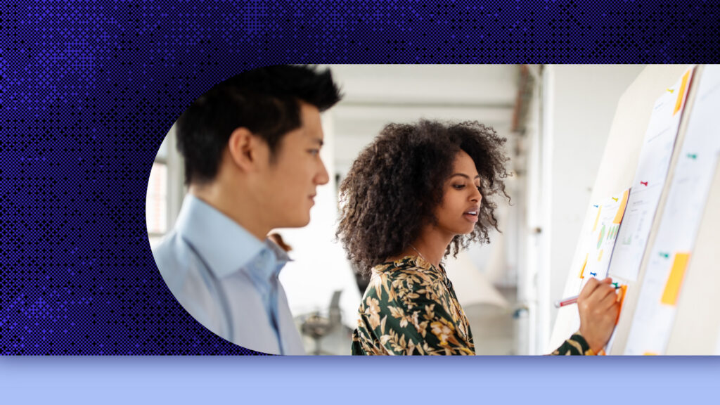 Two employees work together on a whiteboard.