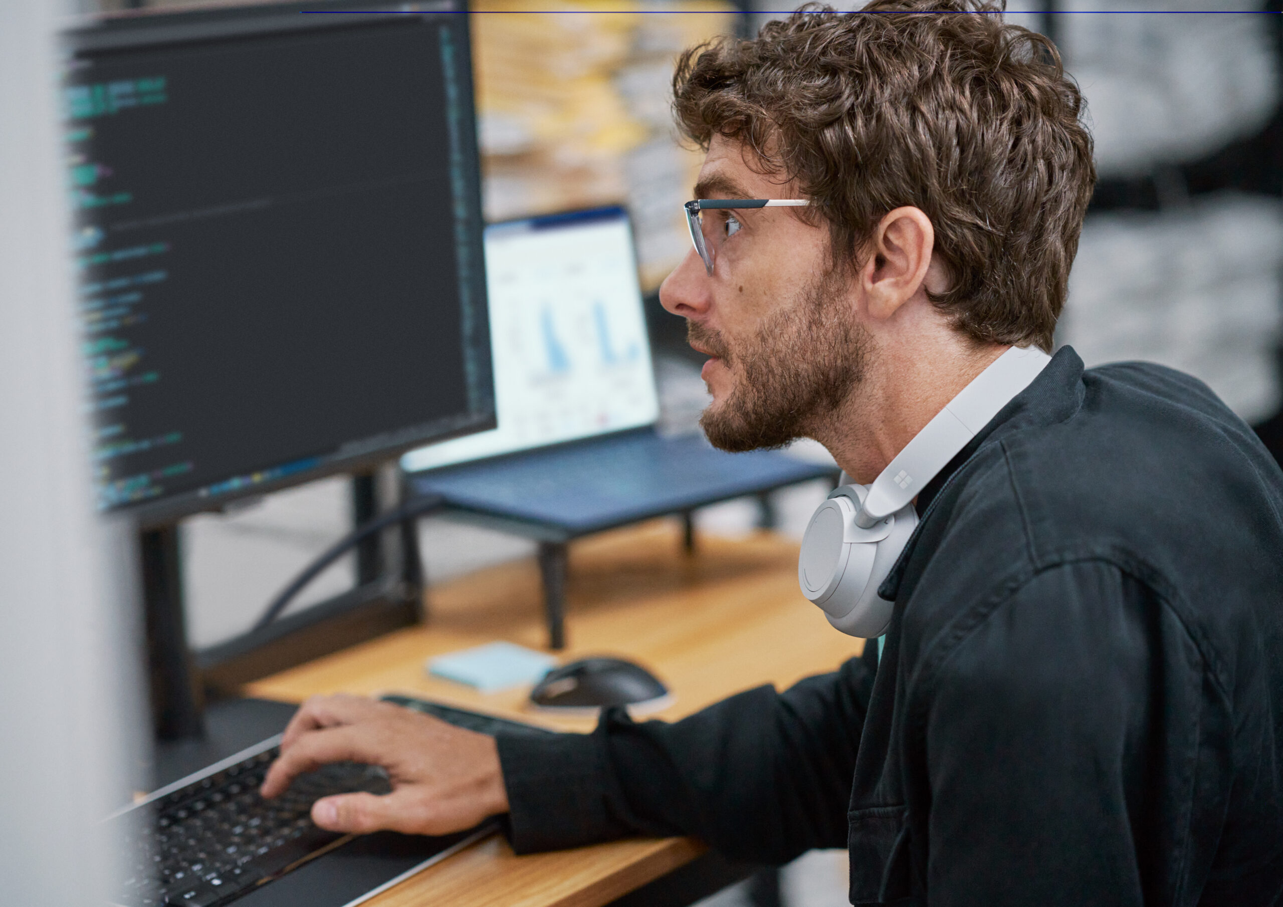 Person sitting at a desk with headphones around their neck working on a computer.