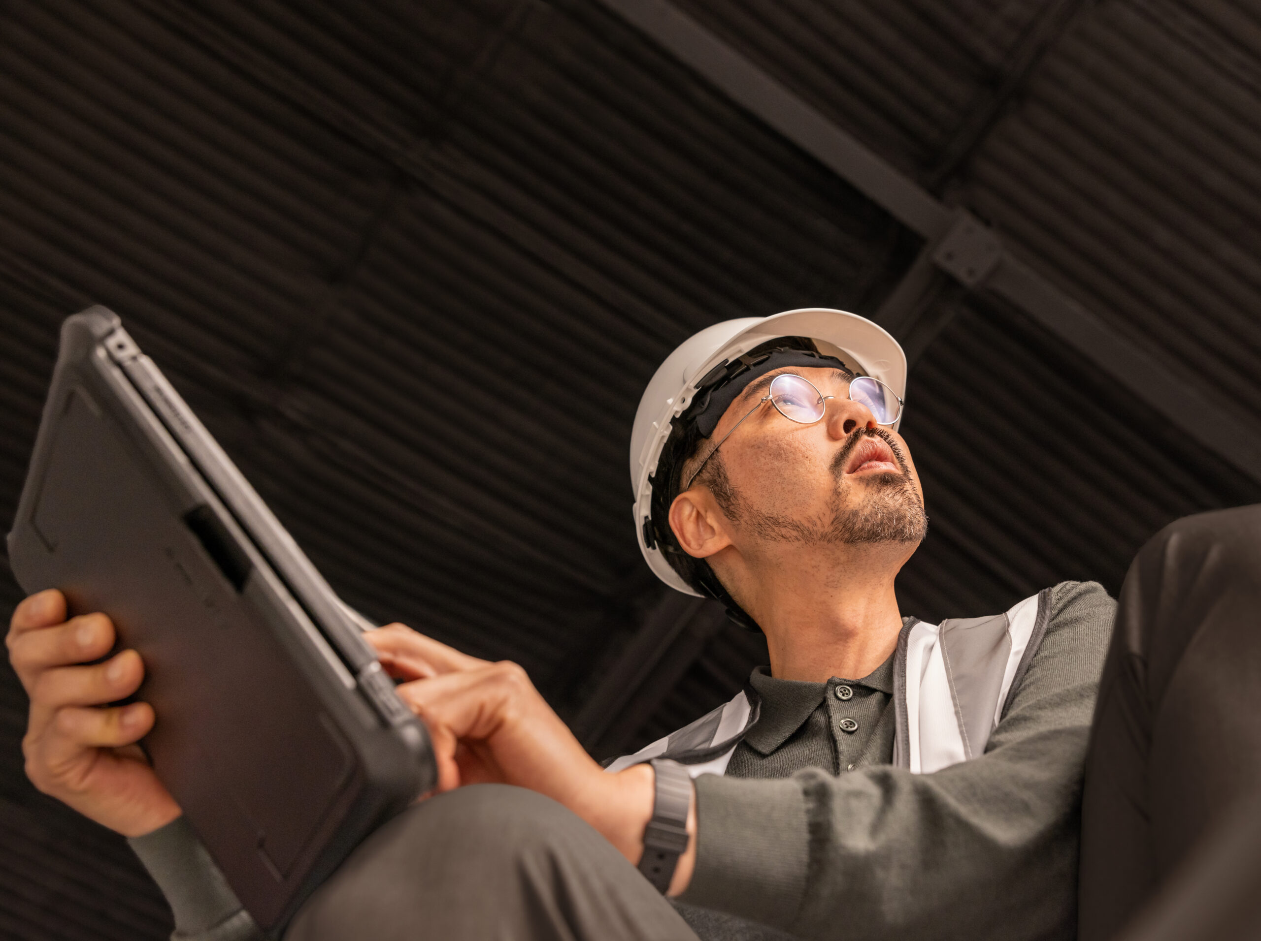 Person wearing a hard hat and safety vest using a tablet inside an industrial facility.
