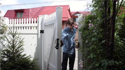 Video of a man opening the door to a white gate and walking through the opening.